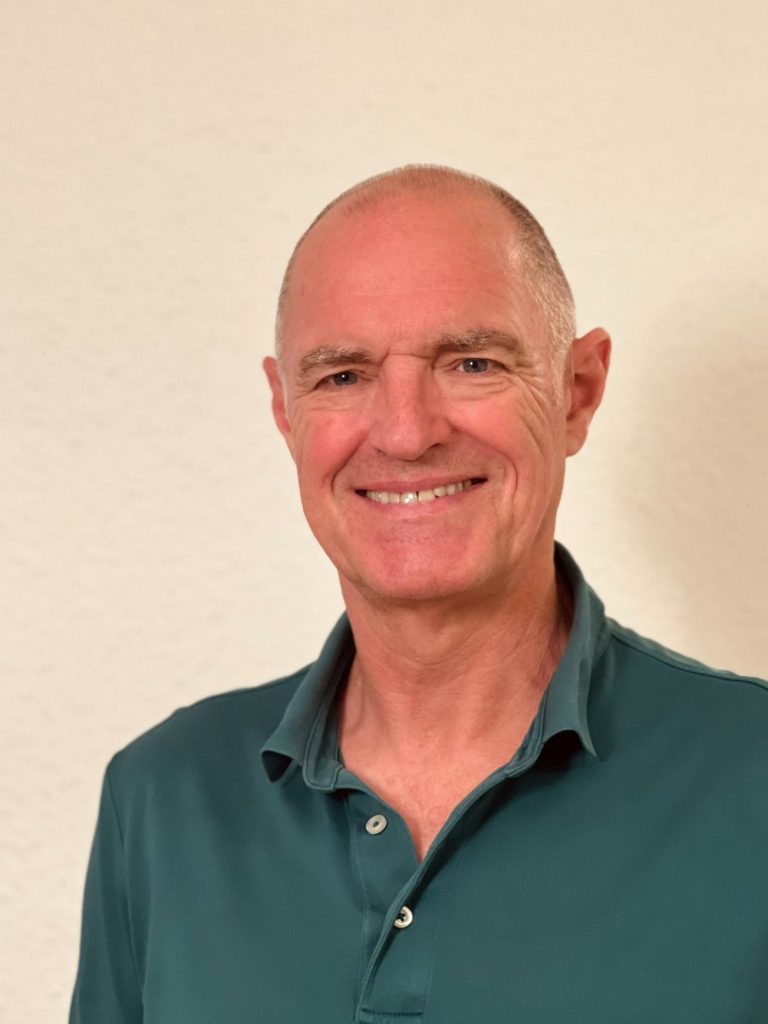 Wim Hermanns Osteopath Heipraktiker Mann mit kurzem Haarschnitt ,Wim Hermanns trägt ein grünes Poloshirt, lächelt freundlich vor neutralem Hintergrund.