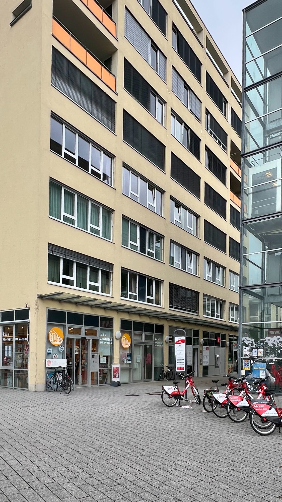 Praxis Eingang Paula-Modersohn-Plat 3, Freiburg-Vauban, Modernes Gebäude mit Geschäftsflächen im Erdgeschoss und Fahrrädern vor dem Eingang.